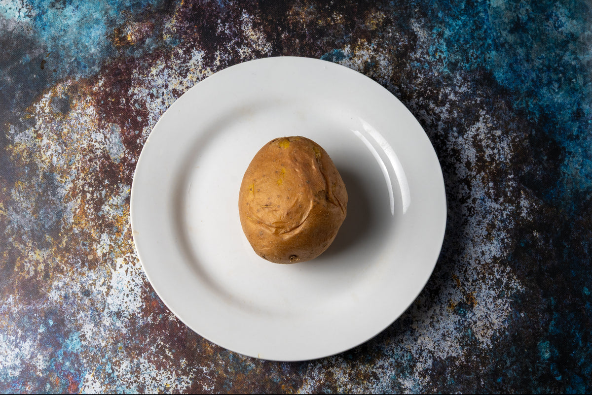 Single potatoe on a white plate against a textured dark background