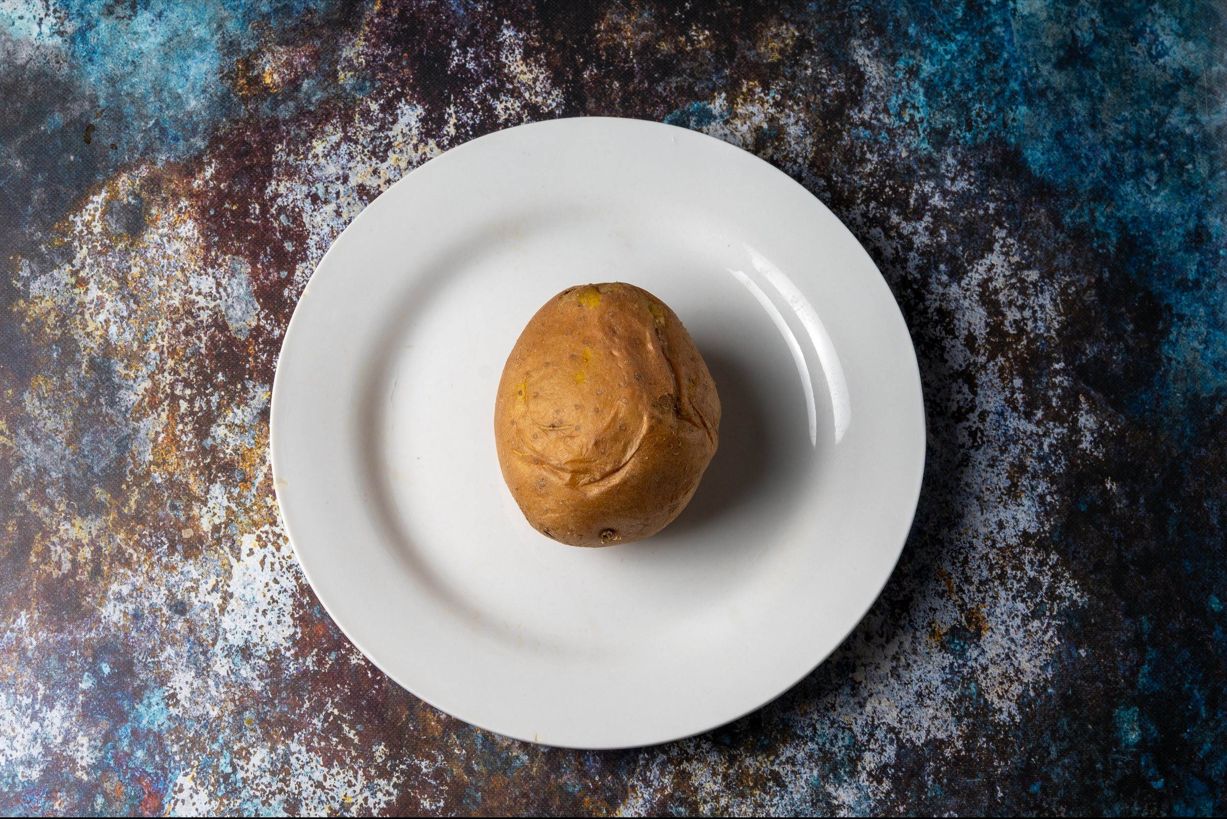 Single potatoe on a white plate against a textured dark background