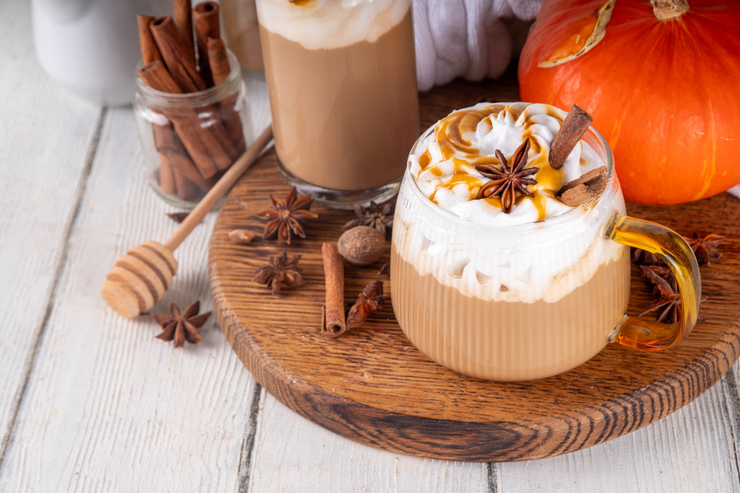 Pumpkin spice latte with whipped cream, cinnamon, and a honey dipper on a wooden coaster.